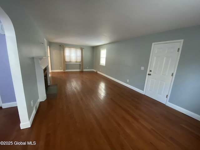 unfurnished living room with dark wood-style floors, a glass covered fireplace, arched walkways, and baseboards