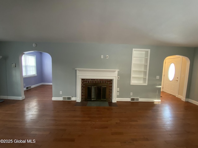 unfurnished living room featuring arched walkways, a fireplace, wood finished floors, and visible vents