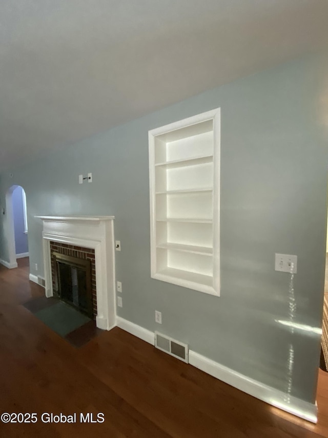 unfurnished living room featuring visible vents, arched walkways, baseboards, a brick fireplace, and built in shelves