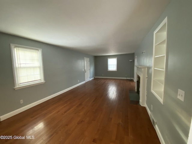 unfurnished living room with visible vents, baseboards, dark wood-style floors, a fireplace with flush hearth, and built in shelves