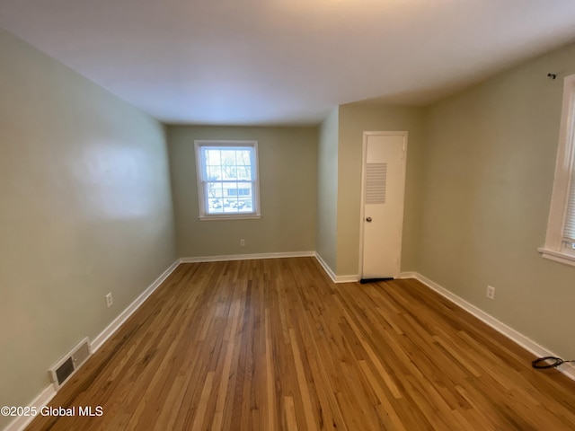 empty room with wood-type flooring, visible vents, and baseboards