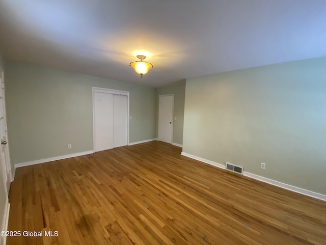 unfurnished bedroom featuring baseboards, a closet, visible vents, and wood finished floors