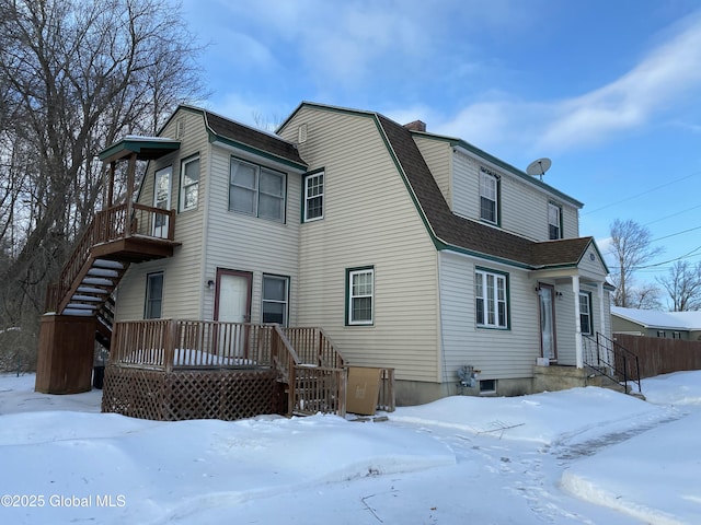 snow covered back of property with a shingled roof, a deck, and a gambrel roof