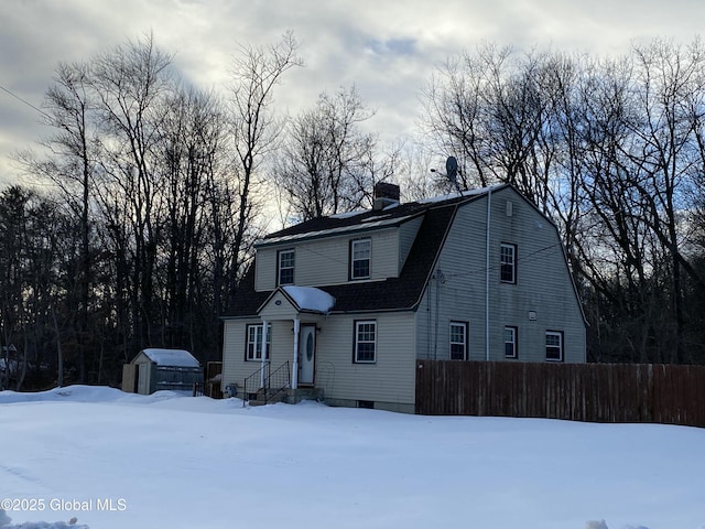 colonial inspired home featuring an outdoor structure, fence, a gambrel roof, and a storage unit