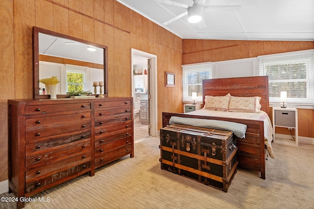 carpeted bedroom featuring ensuite bath, wooden walls, vaulted ceiling, and ceiling fan