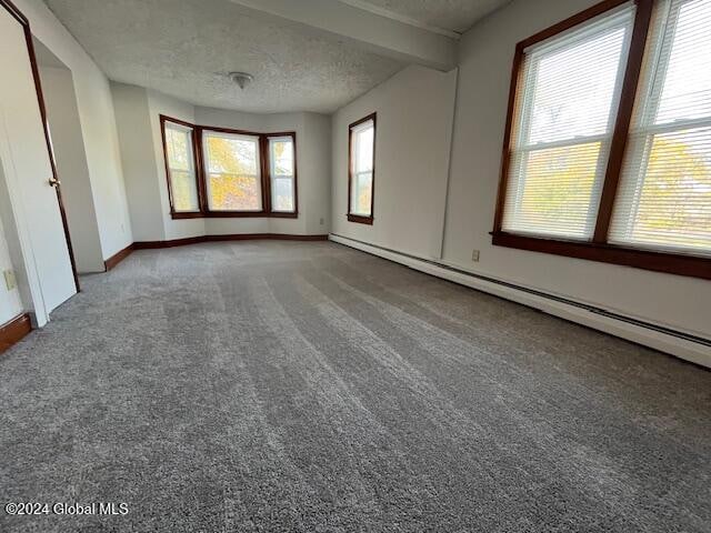 carpeted spare room with a textured ceiling, beamed ceiling, and a wealth of natural light