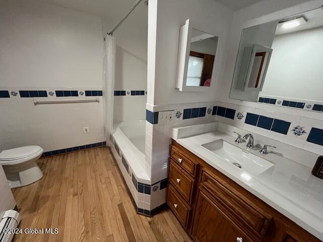 full bathroom with toilet, hardwood / wood-style flooring, shower / bath combo with shower curtain, and baseboard heating