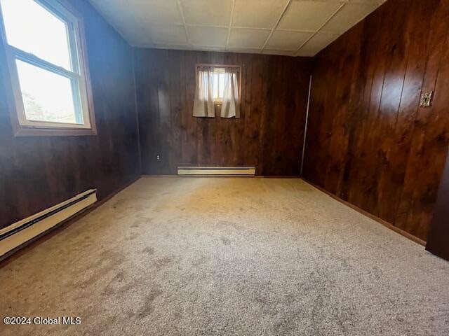 unfurnished room with a baseboard radiator, wooden walls, carpet flooring, and plenty of natural light