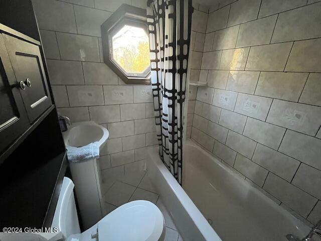 full bathroom with toilet, shower / bathtub combination with curtain, sink, and tile walls