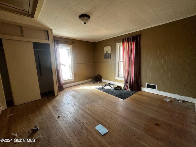 unfurnished bedroom featuring ornamental molding, wood-type flooring, wooden walls, and a closet