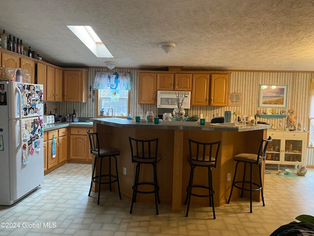 kitchen with a skylight, a kitchen island, white refrigerator, and a kitchen breakfast bar