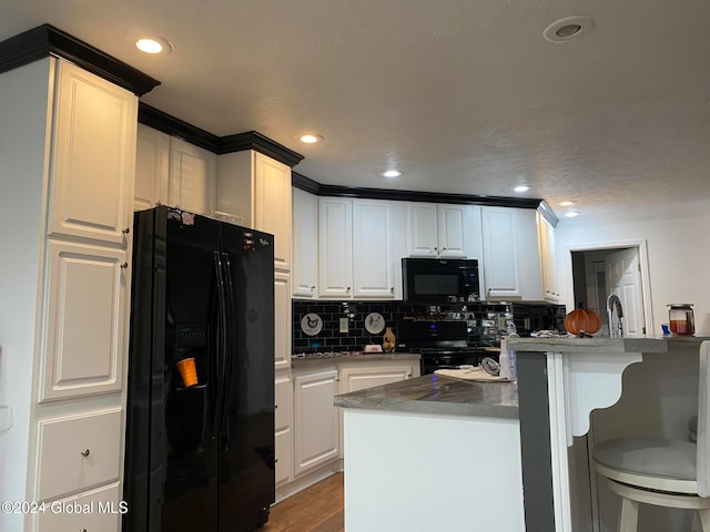 kitchen with white cabinetry, black appliances, a kitchen bar, and a kitchen island