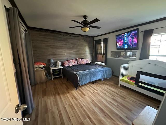 bedroom with ceiling fan, crown molding, wood-type flooring, and wooden walls