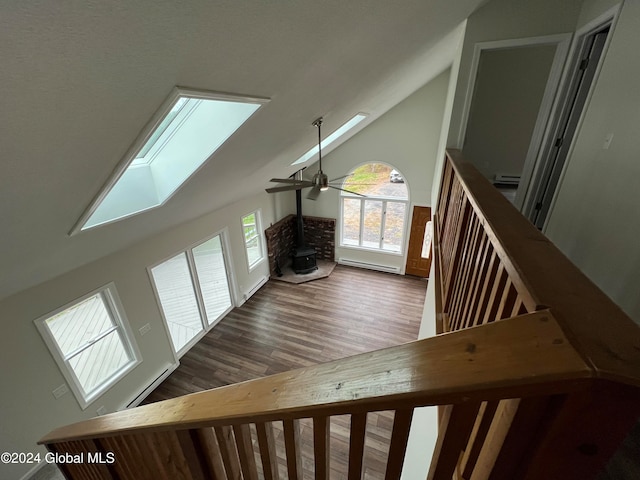 additional living space with vaulted ceiling with skylight, a wood stove, ceiling fan, and dark hardwood / wood-style flooring