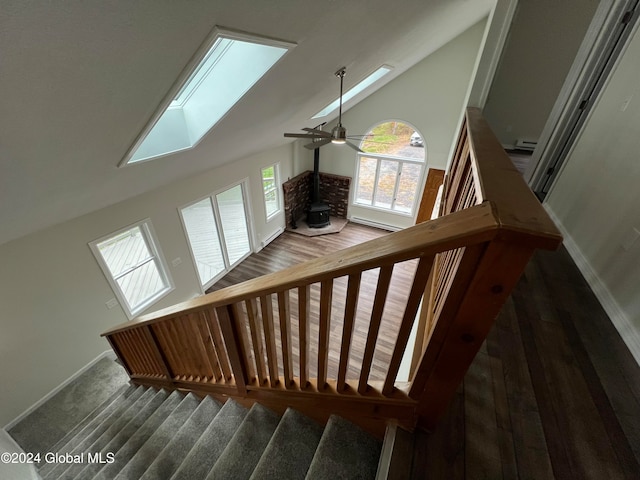 stairs with hardwood / wood-style floors, ceiling fan, a wood stove, and a skylight