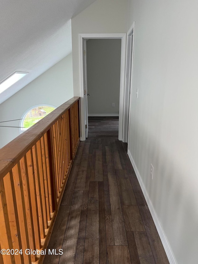 corridor with vaulted ceiling with skylight, dark hardwood / wood-style floors, and a textured ceiling