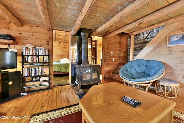 sitting room with wood walls, a wood stove, beamed ceiling, wooden ceiling, and hardwood / wood-style flooring