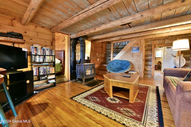 living room featuring beam ceiling, wooden ceiling, wood-type flooring, a wood stove, and wooden walls