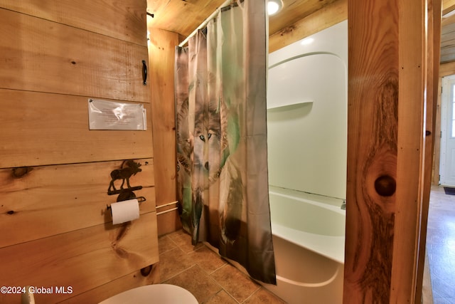 bathroom with toilet, shower / bathtub combination with curtain, and wooden walls