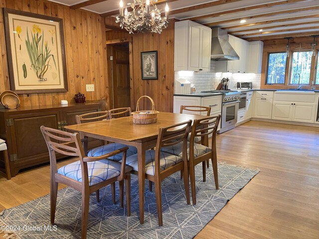 dining space with beamed ceiling, wood walls, sink, and light wood-type flooring