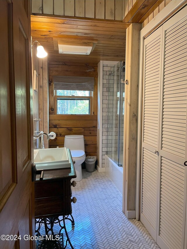 full bathroom featuring vanity, wooden walls, shower / bath combination with glass door, and toilet