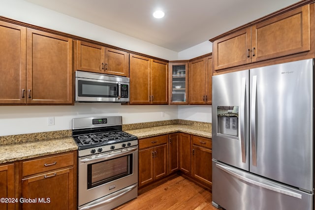 kitchen with light stone countertops, light wood-type flooring, and appliances with stainless steel finishes