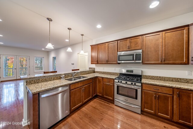 kitchen with stainless steel appliances, sink, kitchen peninsula, decorative light fixtures, and light wood-type flooring