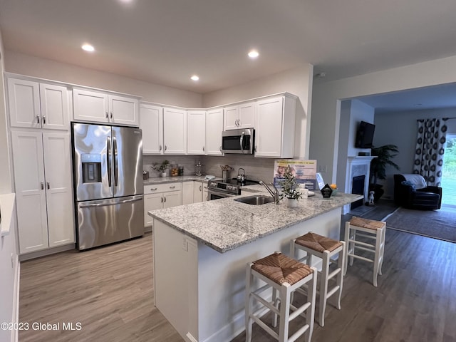 kitchen featuring a peninsula, light wood-style floors, white cabinets, a sink, and appliances with stainless steel finishes