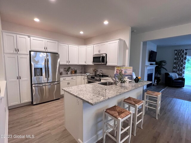 kitchen featuring kitchen peninsula, white cabinets, a kitchen bar, light wood-type flooring, and stainless steel appliances