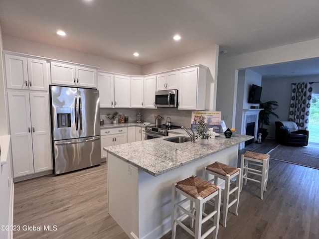 kitchen with a sink, light wood finished floors, stainless steel appliances, white cabinetry, and a peninsula