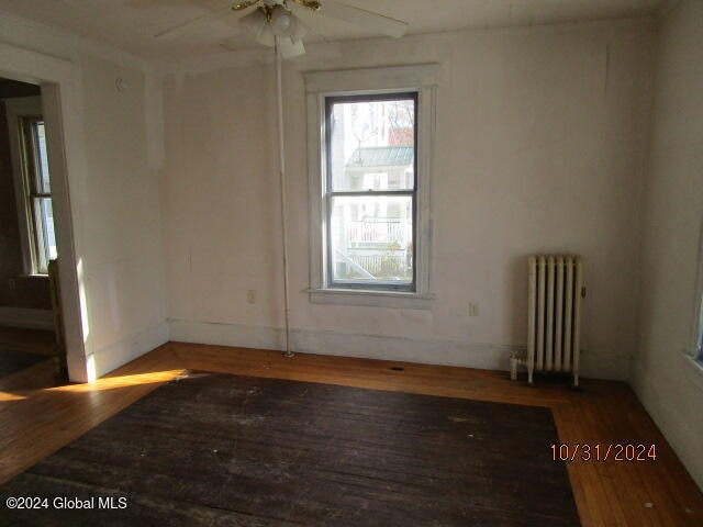 spare room with ceiling fan, wood-type flooring, and radiator