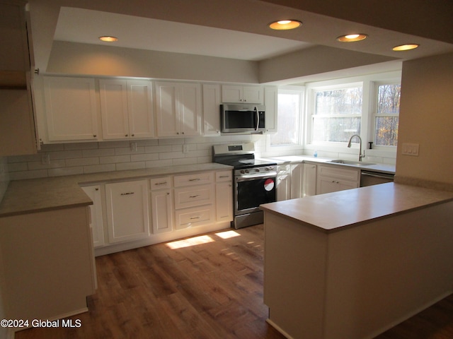 kitchen featuring stainless steel appliances, dark wood-type flooring, kitchen peninsula, sink, and white cabinetry