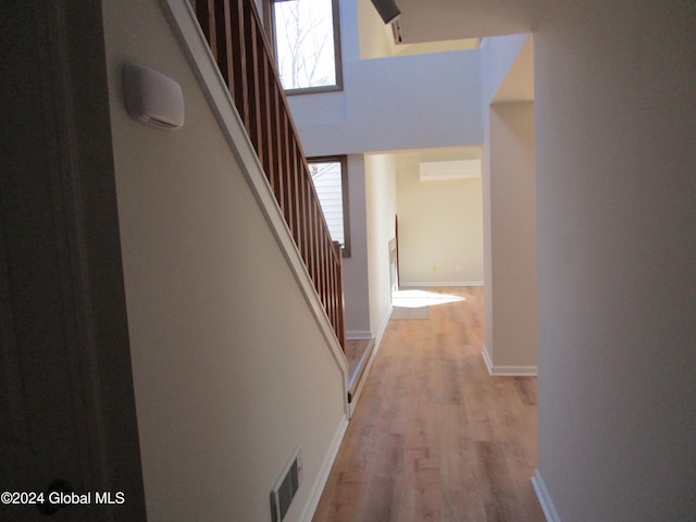 hall with a wall unit AC, a towering ceiling, and light hardwood / wood-style flooring