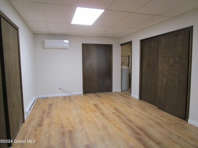 unfurnished bedroom featuring light hardwood / wood-style floors, a wall mounted AC, a paneled ceiling, and multiple closets