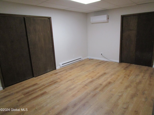 unfurnished bedroom with a wall unit AC, baseboard heating, light wood-type flooring, and a drop ceiling