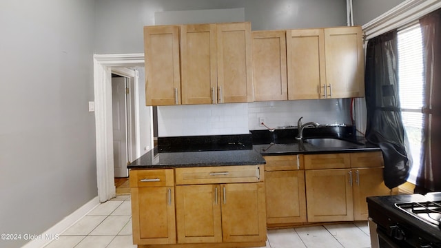 kitchen with sink, stainless steel stove, dark stone countertops, light tile patterned floors, and tasteful backsplash