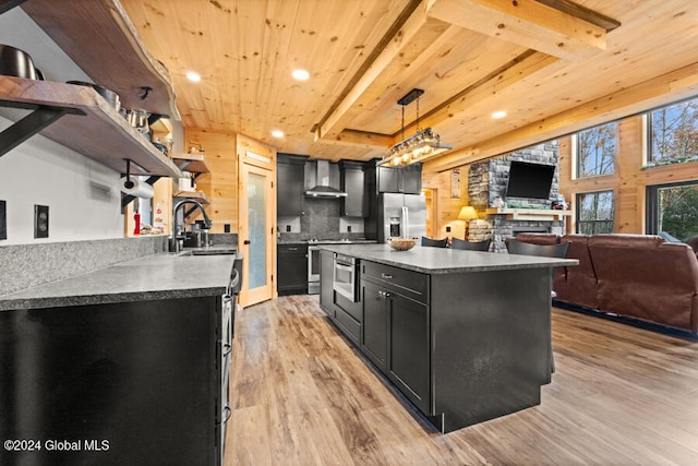 kitchen featuring wall chimney range hood, sink, light wood-type flooring, appliances with stainless steel finishes, and decorative light fixtures