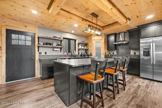 kitchen featuring pendant lighting, a center island, wall chimney exhaust hood, light hardwood / wood-style floors, and stainless steel fridge with ice dispenser