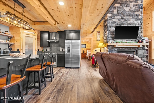 kitchen with dark hardwood / wood-style flooring, wall chimney exhaust hood, wooden walls, pendant lighting, and stainless steel fridge with ice dispenser