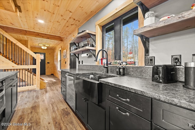 kitchen featuring wood walls, wooden ceiling, sink, light wood-type flooring, and beamed ceiling