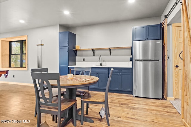 kitchen featuring stainless steel fridge, blue cabinets, sink, a barn door, and light hardwood / wood-style floors