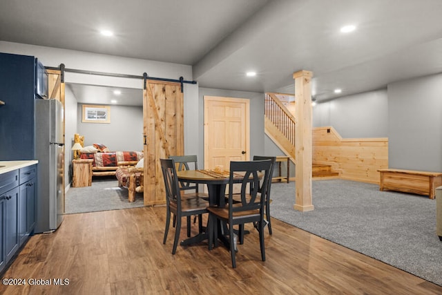 dining space with a barn door, wooden walls, and light hardwood / wood-style floors