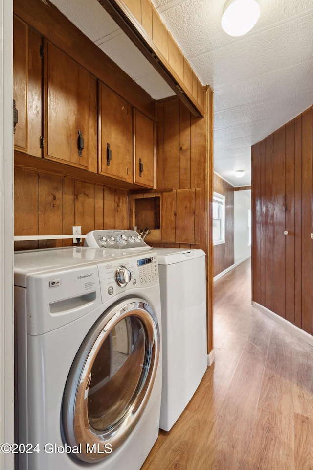 washroom featuring cabinets, a textured ceiling, light wood-type flooring, wood walls, and washing machine and dryer