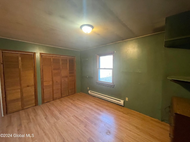 unfurnished bedroom with a baseboard heating unit, light wood-type flooring, and two closets