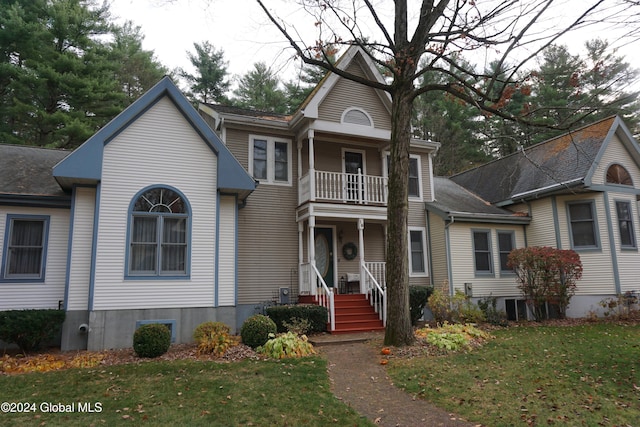 view of front of home with covered porch, a balcony, central AC, and a front yard