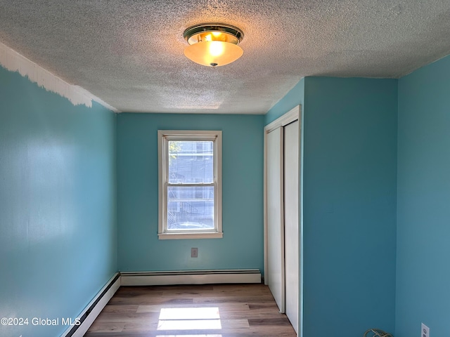 unfurnished bedroom featuring a closet, light wood-type flooring, a textured ceiling, and a baseboard radiator