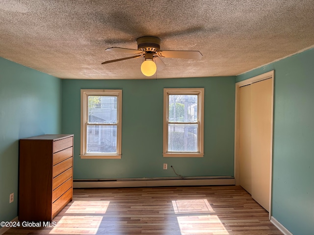 unfurnished bedroom with a closet, a textured ceiling, light hardwood / wood-style floors, baseboard heating, and ceiling fan