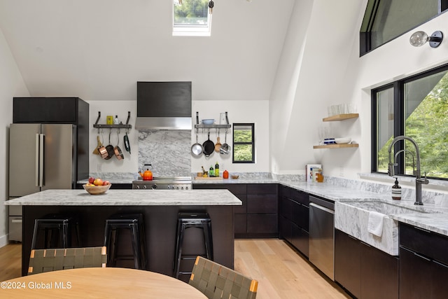 kitchen featuring stainless steel appliances, plenty of natural light, light stone counters, and vaulted ceiling