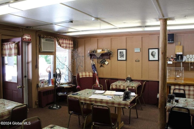 dining space with carpet flooring, wooden walls, a wall mounted air conditioner, and radiator