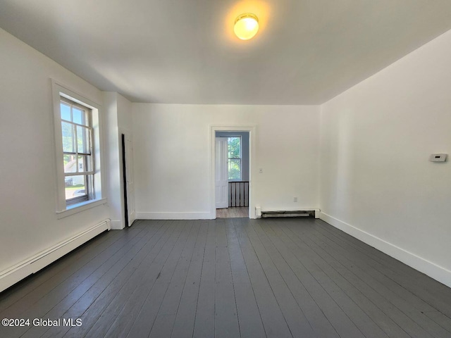 spare room featuring baseboard heating, a wealth of natural light, and dark wood-type flooring